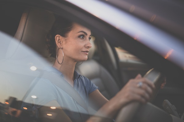 Pretty, young woman  driving a car -Invitation to travel. Car rental or vacation. Nahaufnahme einer Frau am Steuer eines Autos – Konzentrierter Blick, reflektierende Lichter auf der Fensterscheibe und entspannte Fahratmosphäre.