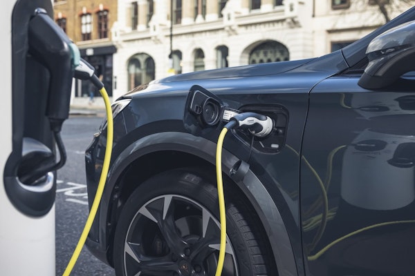 CUPRA Formentor e-Hybrid an einer öffentlichen Ladestation – Nahaufnahme des Ladeanschlusses mit angeschlossenem gelben Ladekabel in urbaner Umgebung.