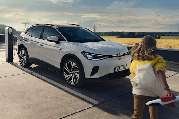 Weißer Volkswagen ID.4 an einer Ladestation auf einem Parkdeck, während ein Kind mit einem Spielzeugflugzeug im Vordergrund läuft – Symbol für nachhaltige Elektromobilität und Freiheit.