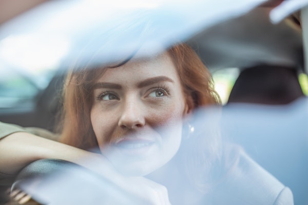Young Woman Embracing Her New Car. Excited young woman and her new car indoors. Young and cheerful woman enjoying new car hugging steering wheel sitting inside Junge Frau sitzt in ihrem neuen Auto