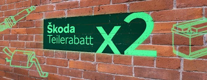 Eine Backsteinwand auf die mit Grafitti Skoda Teilerabatt x2, ein Auspuff, eine Zündkerze und eine Autobatterie gesprüht wurde.