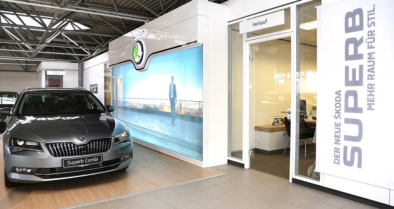 Škoda Superb Combi in der Ausstellung des Autohauses Thiel in Schloß Neuhaus – Moderner Verkaufsbereich mit Glasbüro und Werbebanner für den neuen Superb.